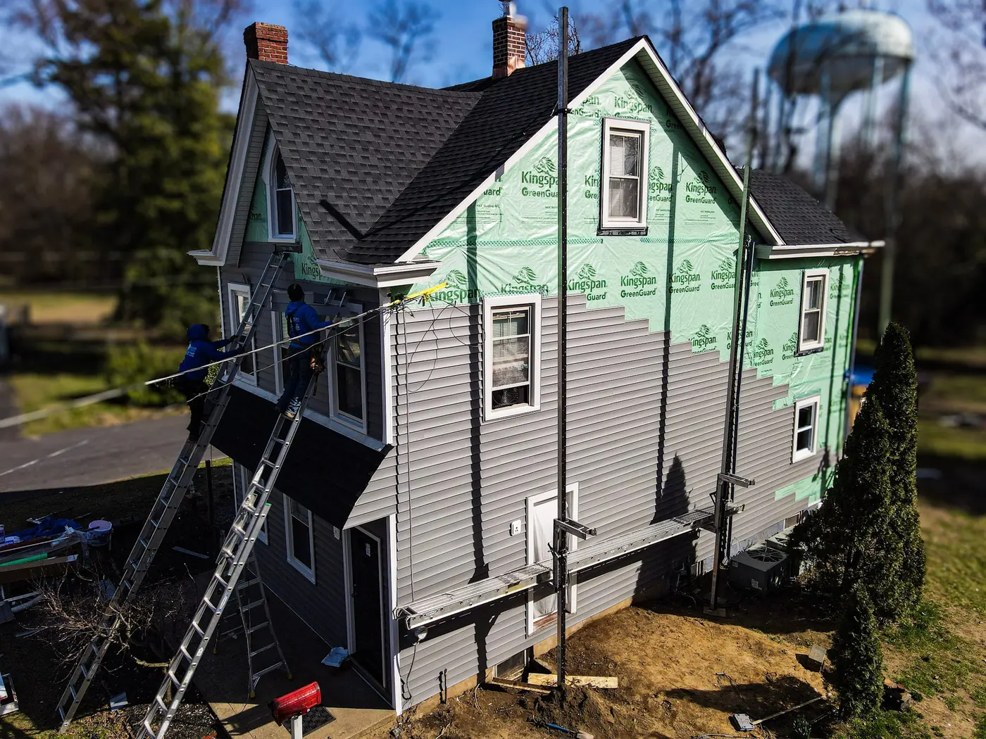 Revolution crew installing grey vinyl siding over green house wrap from ladders